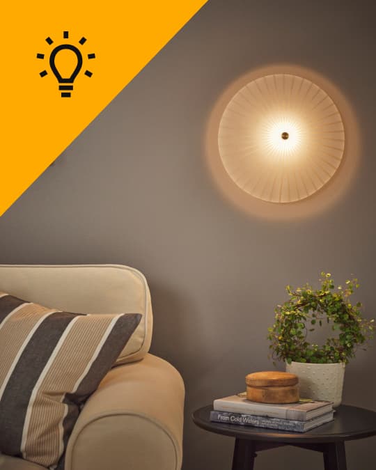 En un livnig, al costado de un sofá una lámpara de pared encendida.