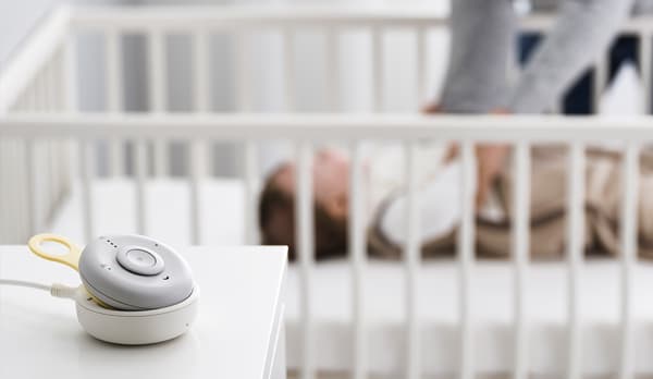 En un primer plano se ve un monitor de seguridad UNDVIKA para escuchar a tu bebé. En el fondo se ve un bebe durmiendo en una cuna.