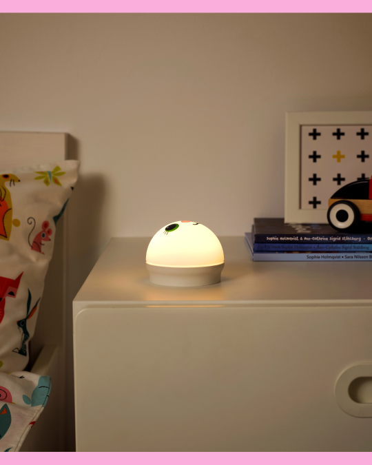En una mesita de noche hay una lámpara infantil con forma de esfera encendida.
