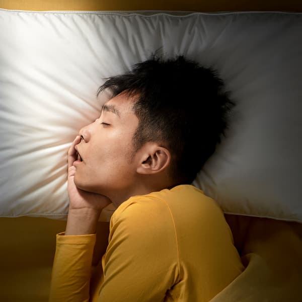 En ung mann ligger på siden og sover dypt på PRAKTVÄDD ergonomisk pute.
