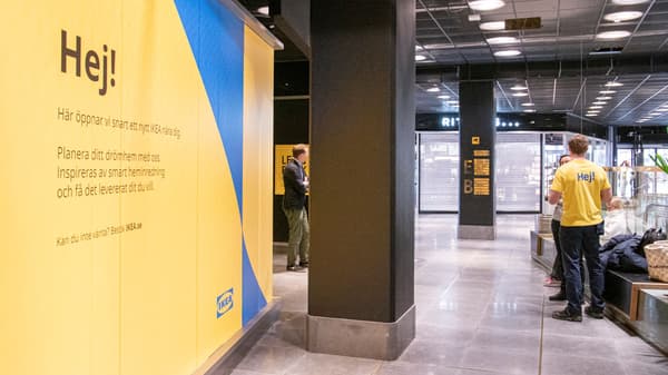 En vägg med gul och blå IKEA-reklam inne i en galleria med en gulklädd person i bakgrunden.