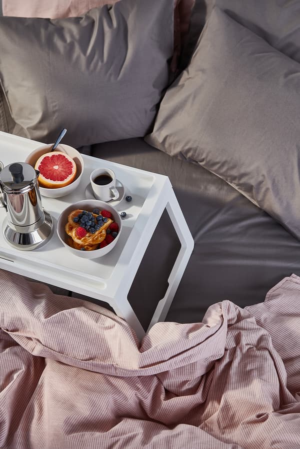 En vit frukostbricka står på en säng. På brickan finns kaffe, våfflor och en grapefrukt. 