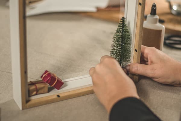 En vit IKEA RIBBA ram med presentband runt under en gran tillsammans med andra inslagna paket.