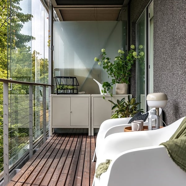 Enclosed balcony with wooden floor, white furniture and green plants