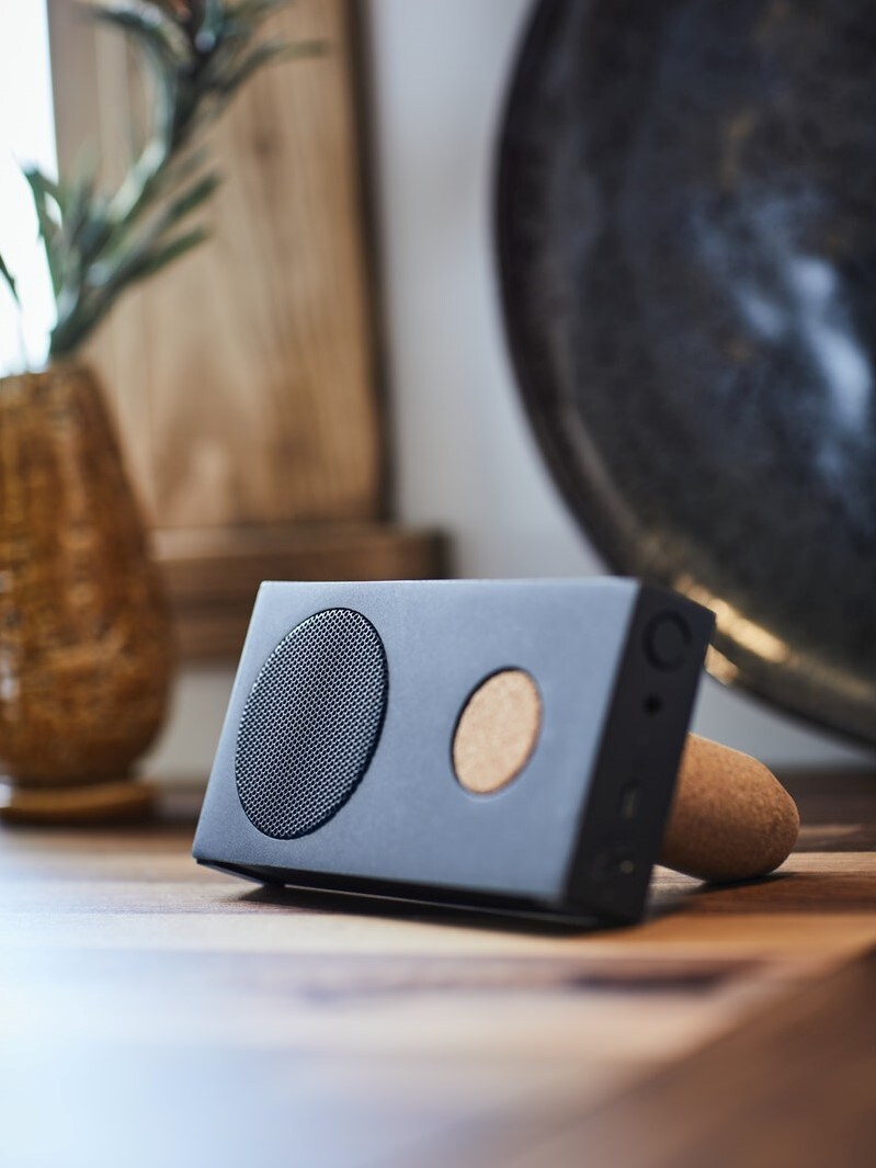 ENEBY Bluetooth reproduktor, černý, s korkovým stojánkem, umístěný na dřevěném stole v moderním interiéru.
