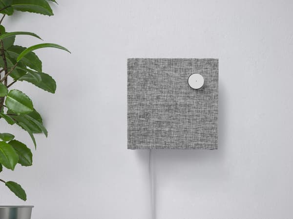 ENEBY Bluetooth speaker wall mounted on a white wall next to a green plant.
