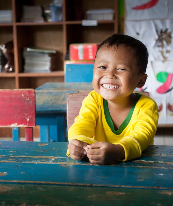 Enfant souriant assis à un bureau bleu.