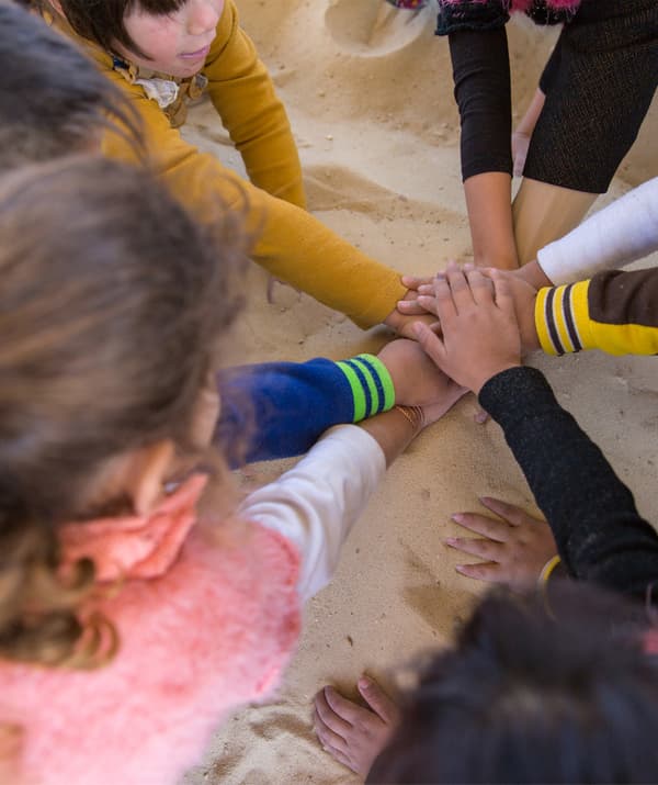 Enfants réunis en cercle et rassemblant leur mains au centre.