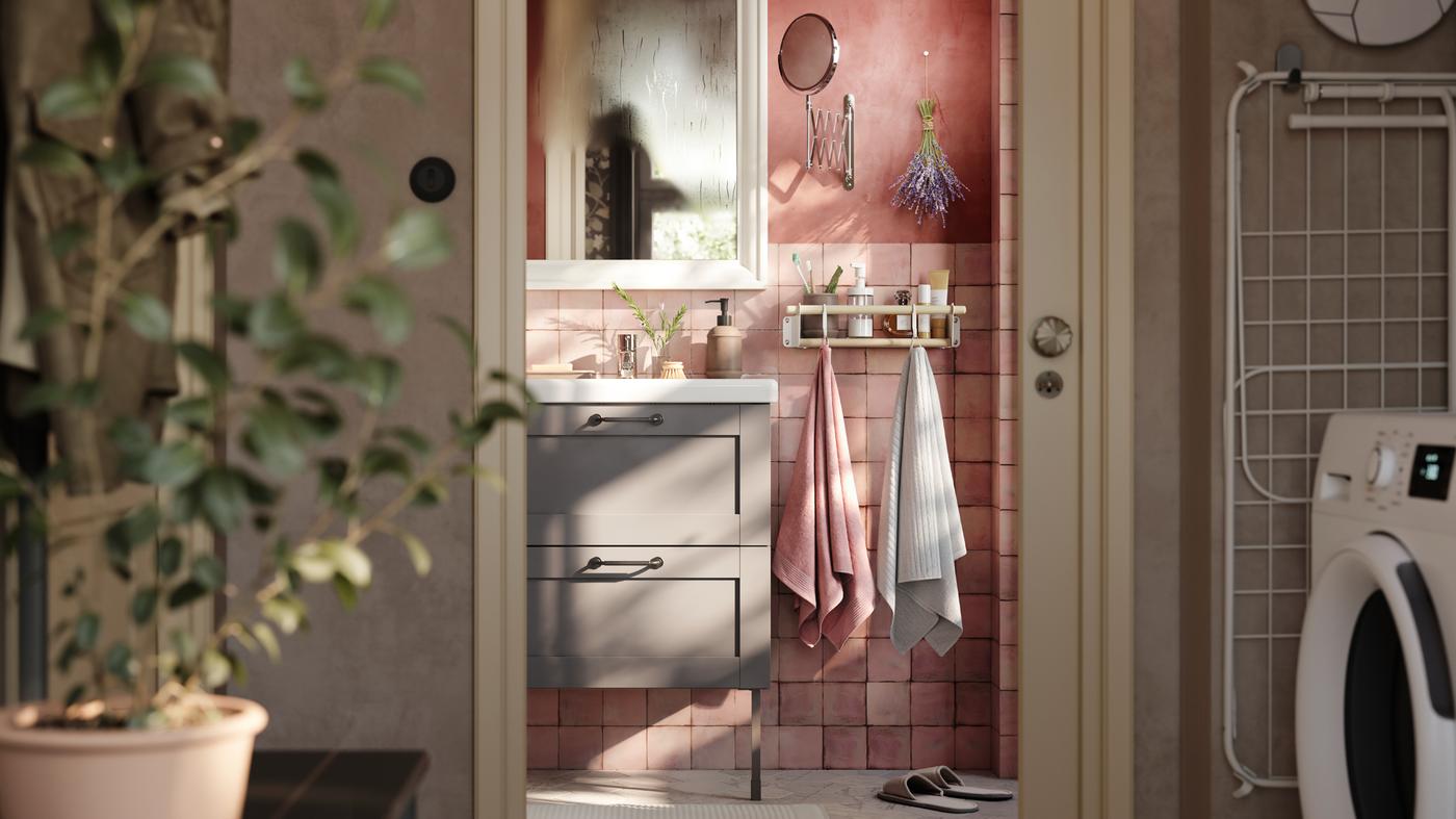 핑크빛 욕실에 그레이 ENHET 엔헤트 2단 하부장 세면대. 화이트 거울과 수건 2장이 후크에 걸려있는 모습.