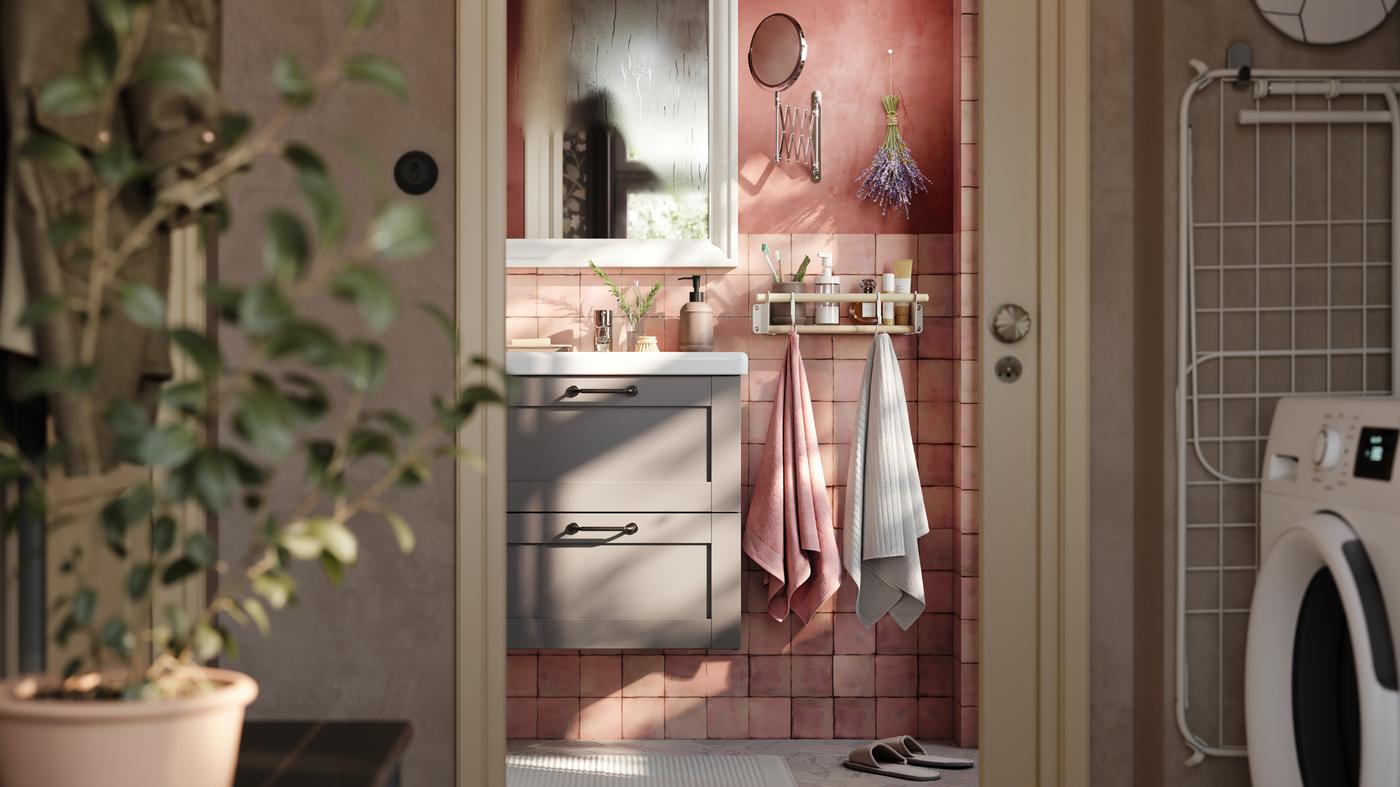 핑크빛 욕실에 그레이 ENHET 엔헤트 2단 하부장 세면대. 화이트 거울과 수건 2장이 후크에 걸려있는 모습.