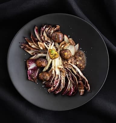 Ensalada de achicoria y nueces con albóndigas vegetales servida en un plato de color gris oscuro, vista desde arriba.
