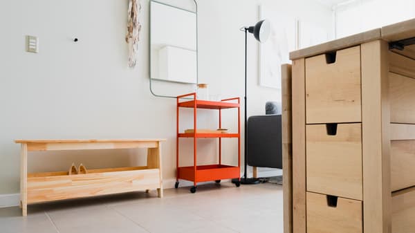 Entrada con un carrito rojo y un zapatero de madera al costado, junto a un espejo de pared.