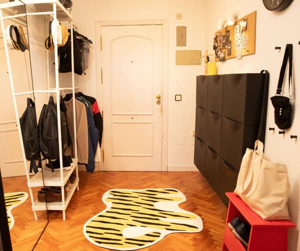 Entrada con zapatero, alfombra, burro con abrigos colgados y taburete de madera.