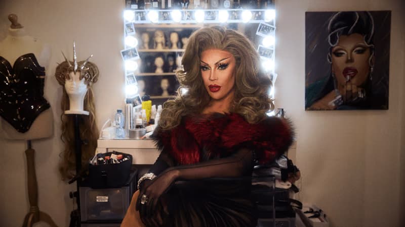 Envy Peru totalmente maquillada y vestida como drag, sentada delante de un espejo con tocador en el vestidor.