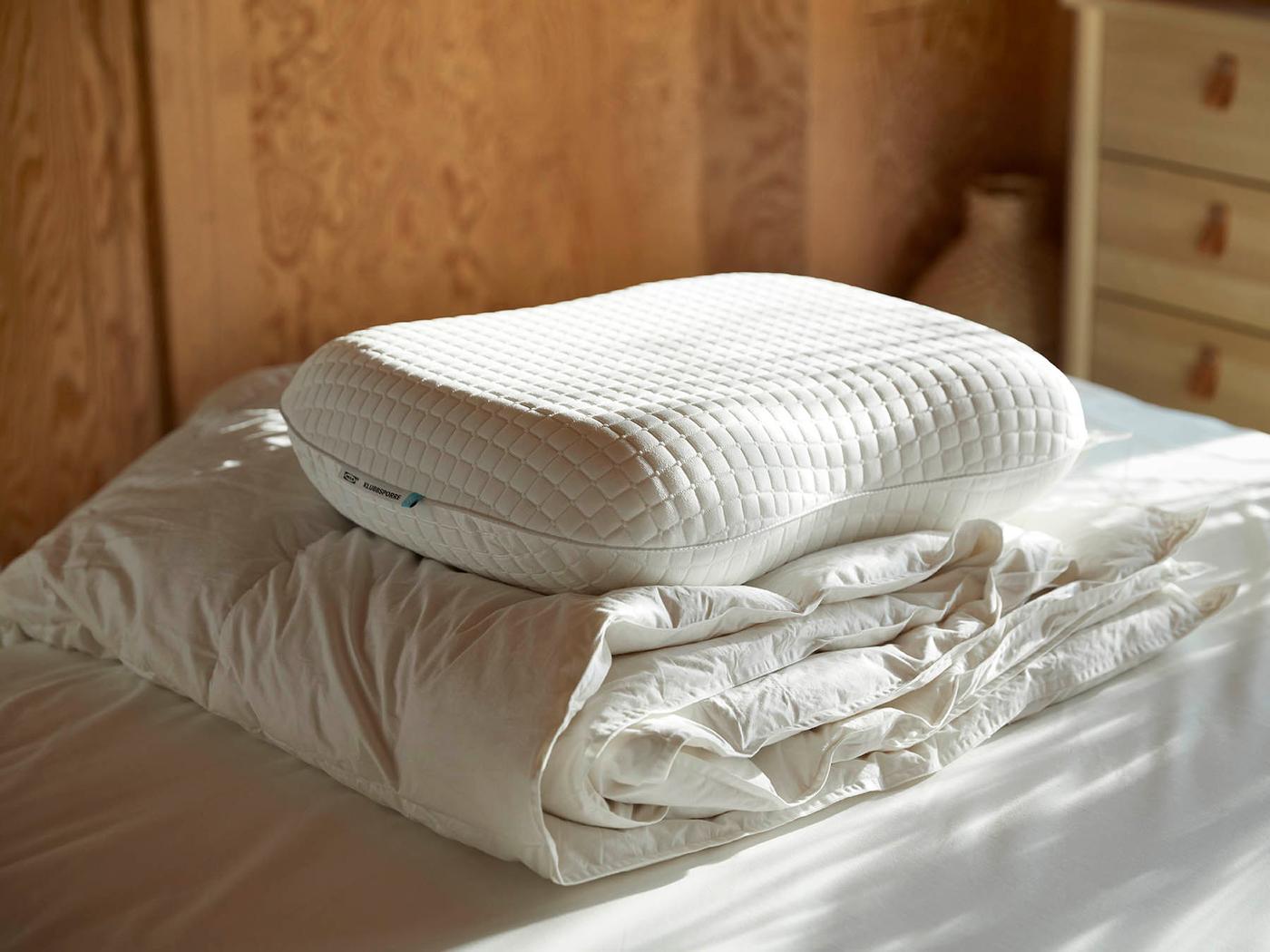 Ergonominen KLUBBSPORRE-tyyny ja lämmin FJÄLLARNIKA-untuvapeitto sängyn päällä.