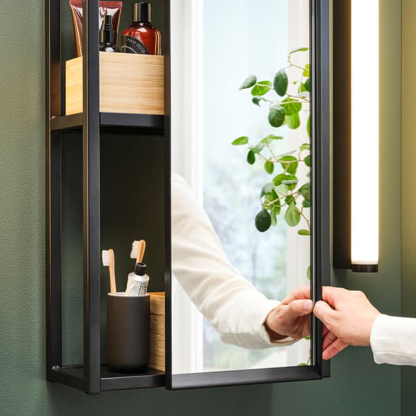 Es ist ein Badezimmer mit einem ENHET Spiegelschrank an der Wand zu sehen.  Auf den Böden befinden sich Toilettenartikel und ein Zahnbürstenhalter.