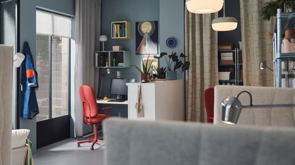 Es ist ein dynamisches Büro mit blauen Wänden, Wandschränken in verschiedenen Farben und SMÖRKULL Drehstühlen mit Armlehnen mit Bezug „Gräsnäs“ in Rot zu sehen.