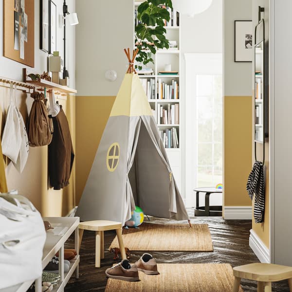 Es ist ein Flur mit zwei LOHALS Teppichen auf dem Boden und einer Reihe HÖVOLM Leisten mit 6 Knöpfen an der Wand zu sehen, an denen Taschen und Hüte hängen.