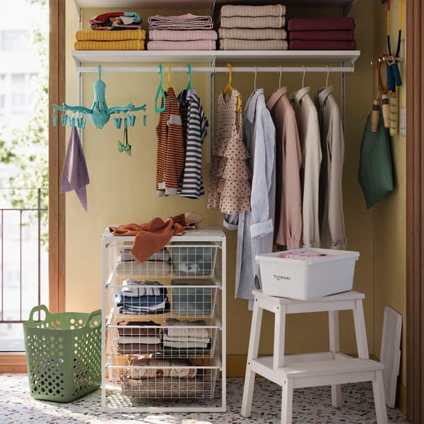 Es ist ein gelbes Badezimmer mit einer weißen BOAXEL Kleiderschrankkombination mit weißen Boxen auf Böden und Kleidung an einer Kleiderstange zu sehen.