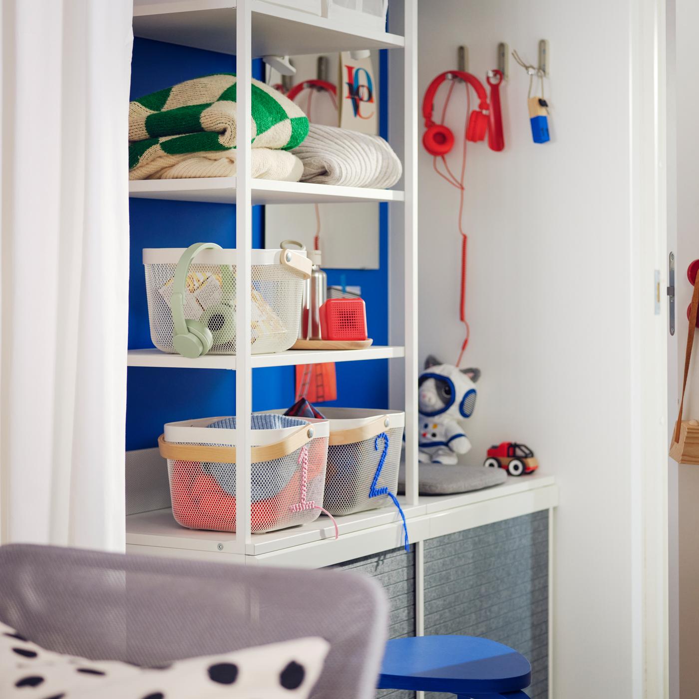 Es ist ein kleiner Flur im Scandi-Stil mit einem offenen weißen PLATSA Kleiderschrank mit Körben und Kleidung auf Böden an einer blauen Wand zu sehen.