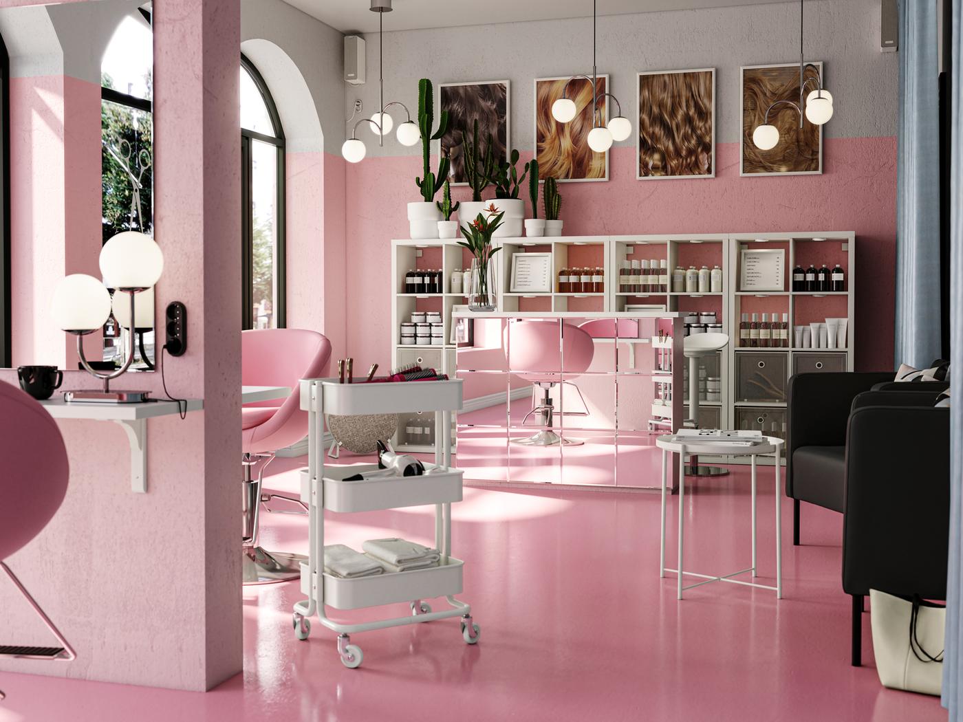 Es ist ein luftiger, in Rosa gehaltener Frisörsalon mit weissen KALLAX Regalen hinter einem Empfangstisch zu sehen. An einem Haarschneideplatz steht ein RÅSKOG Servierwagen.