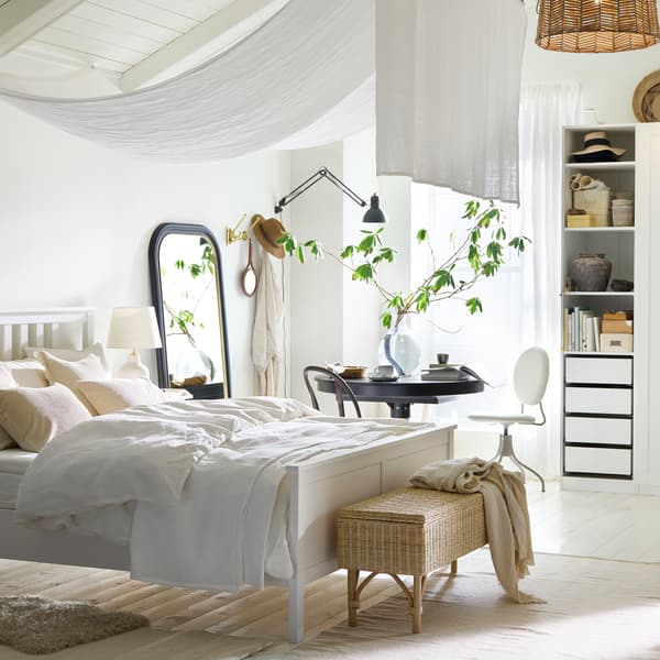 Es ist ein luftiges Schlafzimmer mit einem weißen HEMNES Bettgestell und einem schwarzen INGATORP Ausziehtisch zu sehen, der an einem Fenster steht.