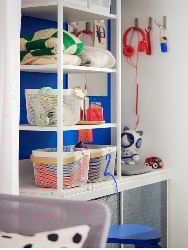 Es ist ein offener weisser PLATSA Kleiderschrank mit dunkelgrauen LARKOLLEN Schiebetüren neben einer Tür zu sehen. In ihm befinden sich Boxen und gefaltete Kleidung.