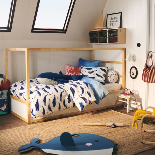 Es ist ein umbaufähiges KURA Bett zu sehen, das mit BLÅVINGAD Bettwäsche mit Walmuster bezogen ist. Darauf liegt ein BLÅVINGAD Stoffspielzeug in Form eines Blauwals.