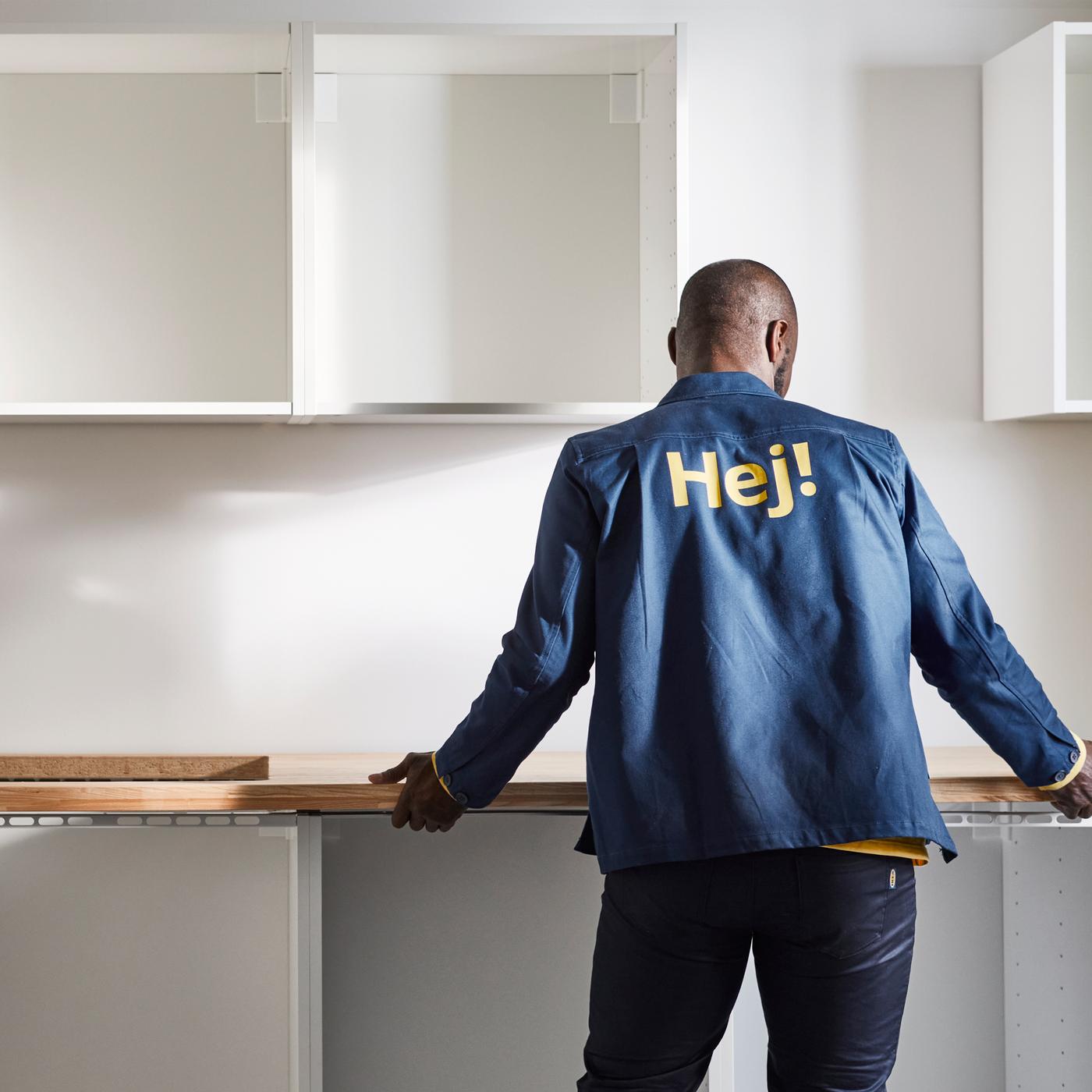 Es ist eine Person in einer blauen Jacke zu sehen, die eine weiße Küche mit Unter- und Wandschränken und einer Laminatarbeitsplatte in Eichenachbildung installiert.