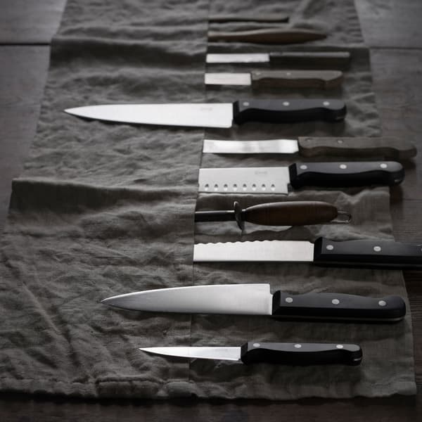 Es ist eine schwarze Messerrolle mit etwa 10 Messern darin zu sehen. Einige von ihnen stecken in ihren Taschen, andere liegen obenauf.