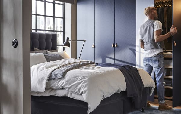 Escena de un dormitorio con un hombre de pie frente a un armario abierto.