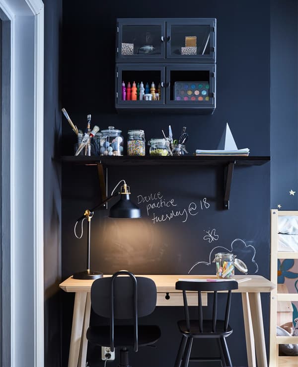 Escritorio compartido para el padre y el niño. Los estantes oscuros están montados en la pared oscura sobre el escritorio de madera y dos sillas de trabajo.