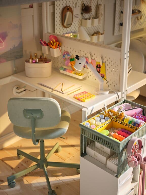 Escritorio infantil con carrito organizador, silla verde claro y objetos de estudio.