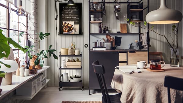 Espace cuisine et salle à manger chaleureux avec étagères ouvertes, table en bois, plantes, suspensions et ambiance conviviale.