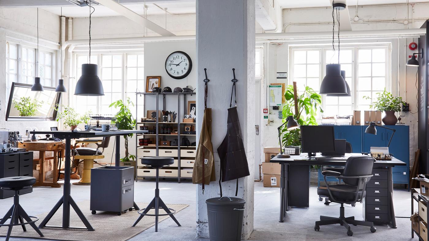 Espace de bureau avec des tabourets réglables, des bureaux assis/debout, des rangements, des suspensions, des objets divers et de la verdure.
