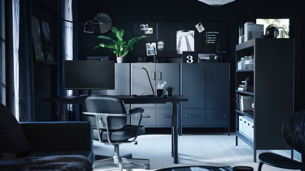 Espace de bureau moderne dans les tons foncés comprenant un bureau, une chaise, un écran d’ordinateur, et divers éléments de rangement et étagères
