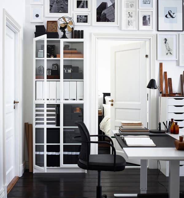 Espace de travail à domicile présentant du rangement, quantité d’œuvres exposées au mur, un bureau et une chaise.