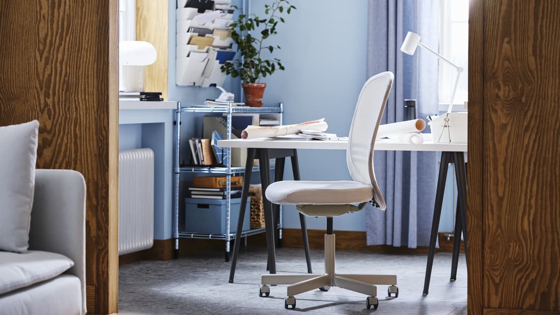 Espace de travail aux murs bleus meublé d’un bureau, d’une chaise pivotante FLINTAN beige, et d’une étagère zinguée avec des boîtes de rangement et une plante.