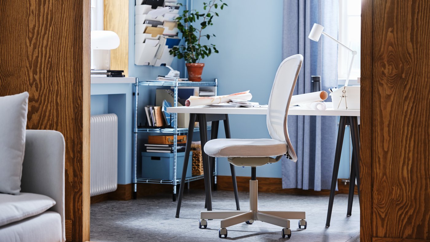 Espace de travail aux murs bleus meublé d’un bureau, d’une chaise pivotante FLINTAN beige, et d’une étagère zinguée avec des boîtes de rangement et une plante.