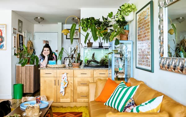 Espace de vie ouvert faisant la part belle aux plantes, avec îlot de cuisine, aquarium, canapé et coussins, table basse et décorations murales.