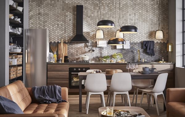 Espace décloisonné comprenant cuisine, salle à manger et séjour, avec des canapés en cuir brun et des armoires de cuisine en bois contre un mur carrelé.