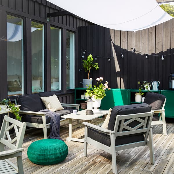 Espace extérieur avec canapé, fauteuils et table basse BONDHOLMEN en gris. Un pouf rond de couleur vert foncé est posé au sol.