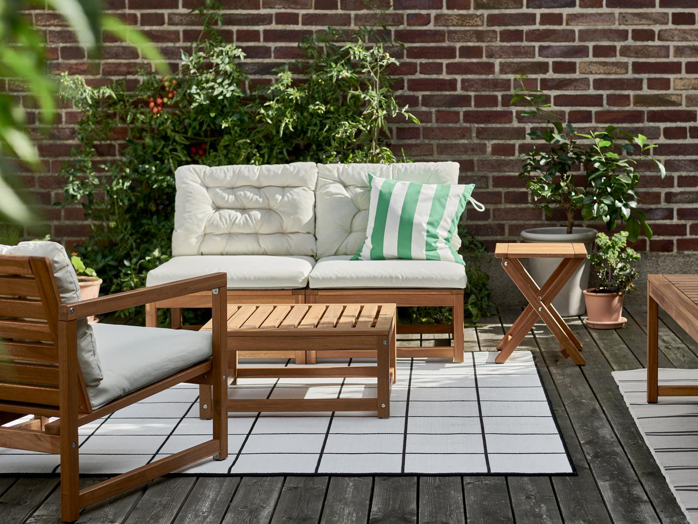 Espace extérieur ensoleillé avec ensemble 4 places NÄMMARÖ sur un tapis, et plantes contre un mur de briques.