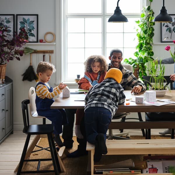 Espaço de refeição com família a brincar à volta da mesa, com cadeiras e candeeiros numa divisão grande, iluminada e arejada.
