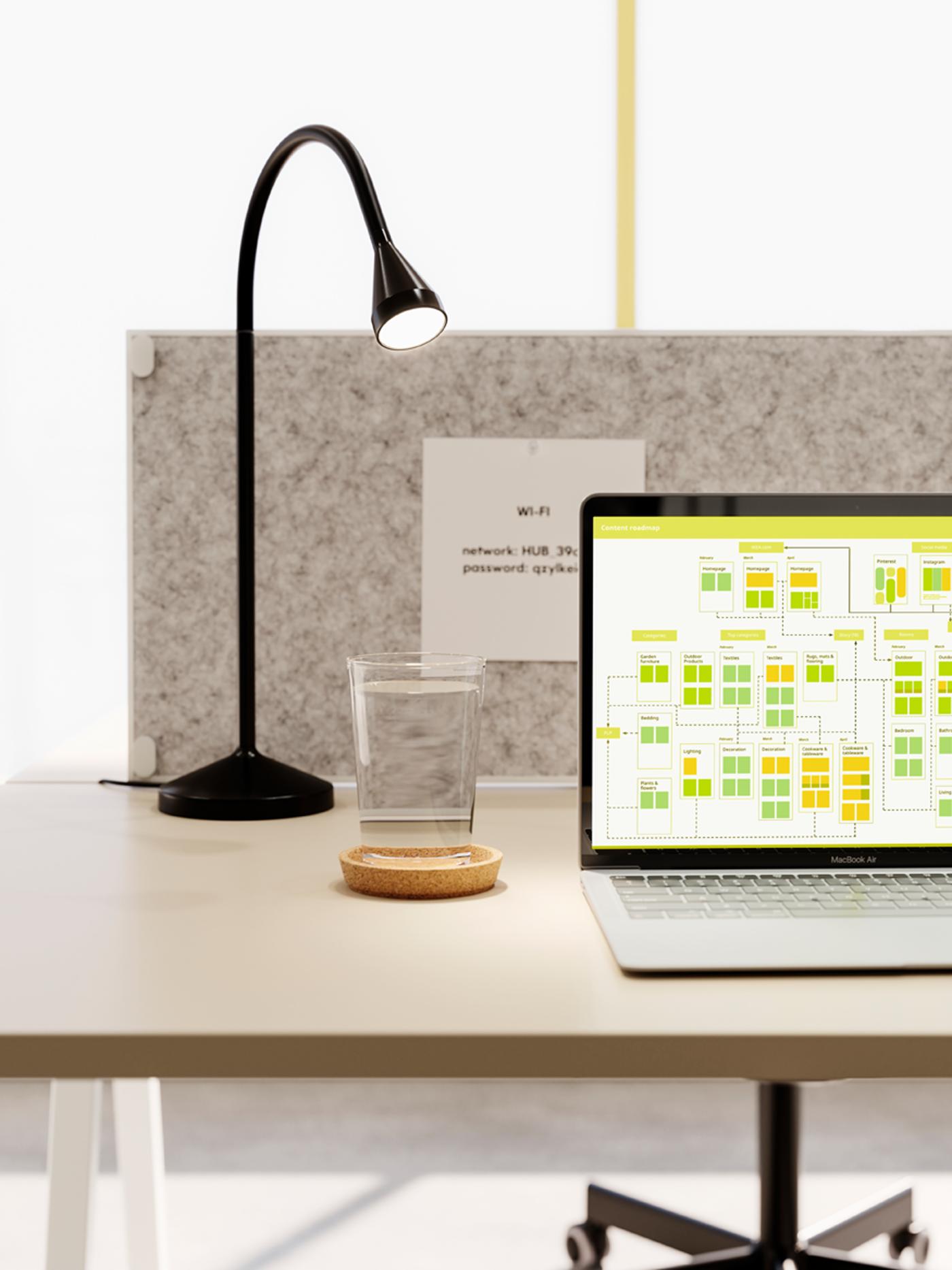 Espaço de trabalho arrumado e minimalista com um computador portátil, um candeeiro LED de secretária NÄVLINGE em preto e um copo de água.