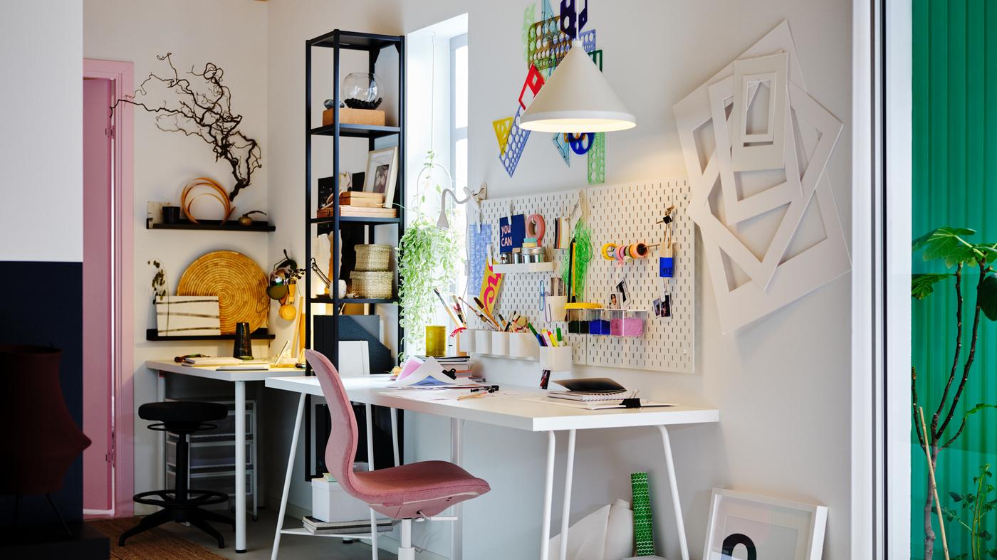 Espaço de trabalho com secretária LAGKAPTEN/TILLSLAG em branco, cadeira giratória LÅNGFJÄLL em castanho rosado claro, placares e candeeiro suspenso.