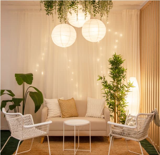 Espai de treball amb escriptoris ajustables blancs, cadires clares, paret amb separador de llistons de fusta i plantes verdes que pengen del sostre.