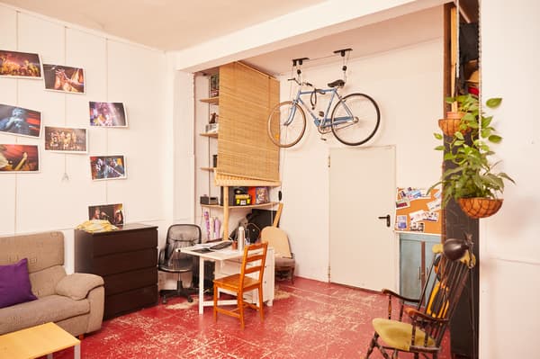 Espai multiús amb mobles diferents: escriptori, sofàs, cadires, butaques, fotos penjades, plantes, prestatgeria coberta i una bicicleta penjada.