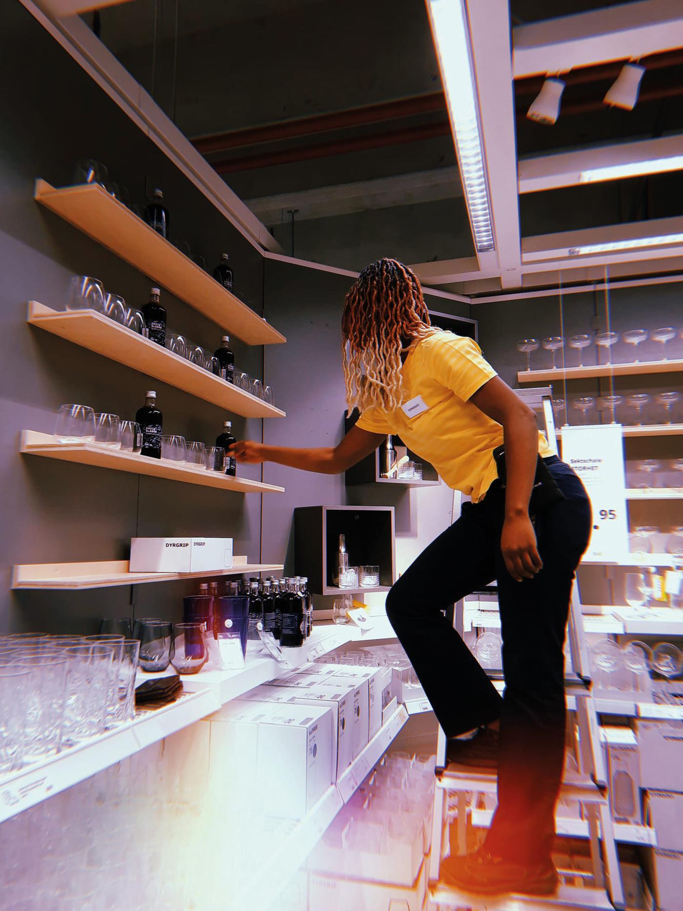 Esperance, réfugiée congolaise et collaboratrice IKEA, debout sur une échelle, tend la main pour attraper un verre.