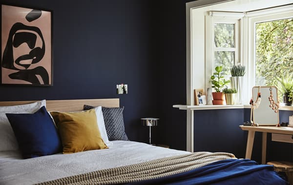 Esquina dun dormitorio azul escuro cunha cama dobre e testos con plantas na repisa da ventá.